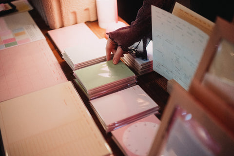 A close-up of someone’s hand picking up pastel-colored notepads from a display of Fluo planners and stationery at Oslos Supermarked.