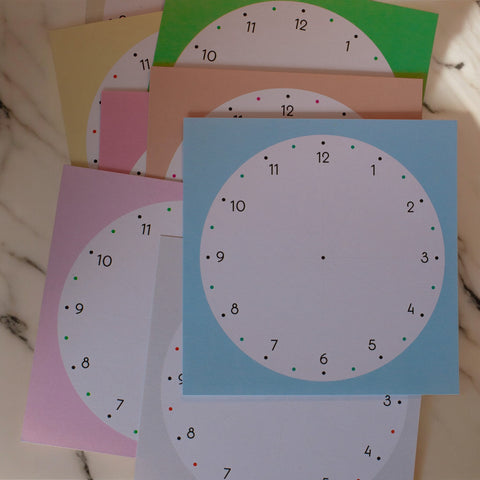 Stack of colorful square memo sheets featuring blank clock faces, designed for visual, analogue routine planning.