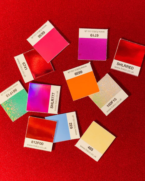 Mini foil swatches in assorted colors and finishes from Foilco, on a velvet deep red background