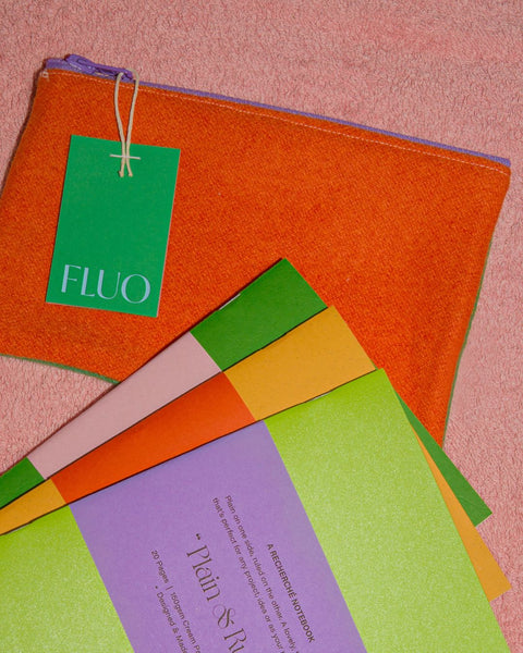 Three notebooks in assorted colors and an orange pencil case, on a pink surface