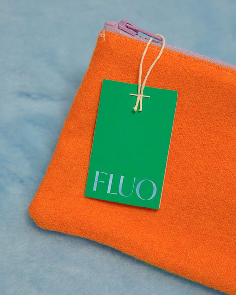 An orange wool pencil case placed on a blue fabric background, with a green, hot-foiled label that reads "Fluo"
