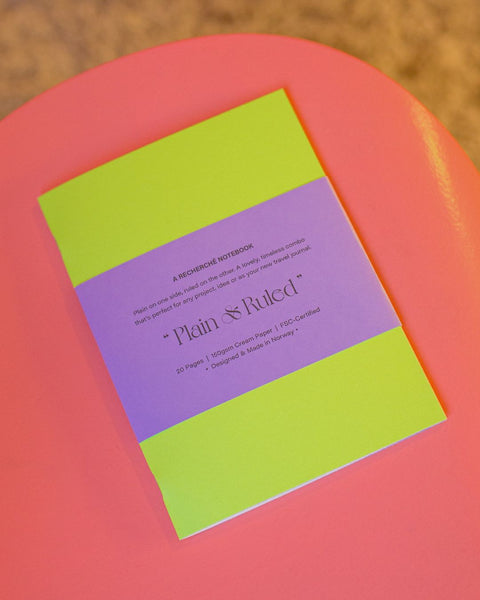 A neon yellow notebook with a lilac belly-band, placed on the surface of a pink chair