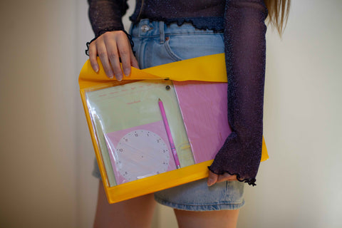 Person wearing a sparkly blue top, holding an A4 general purpose folder from Hightide in yellow, which contains colorful notepads and a pink pencil.