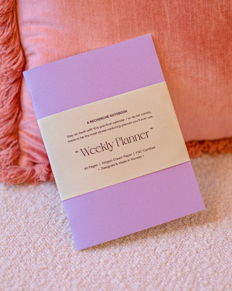 A lilac weekly planner notebook placed on a pink sofa