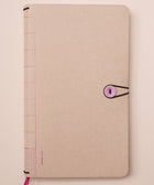Beige notebook with a pink elastic band on a light pink surface