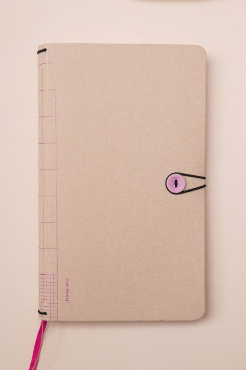 Beige notebook with a pink elastic band on a light pink surface