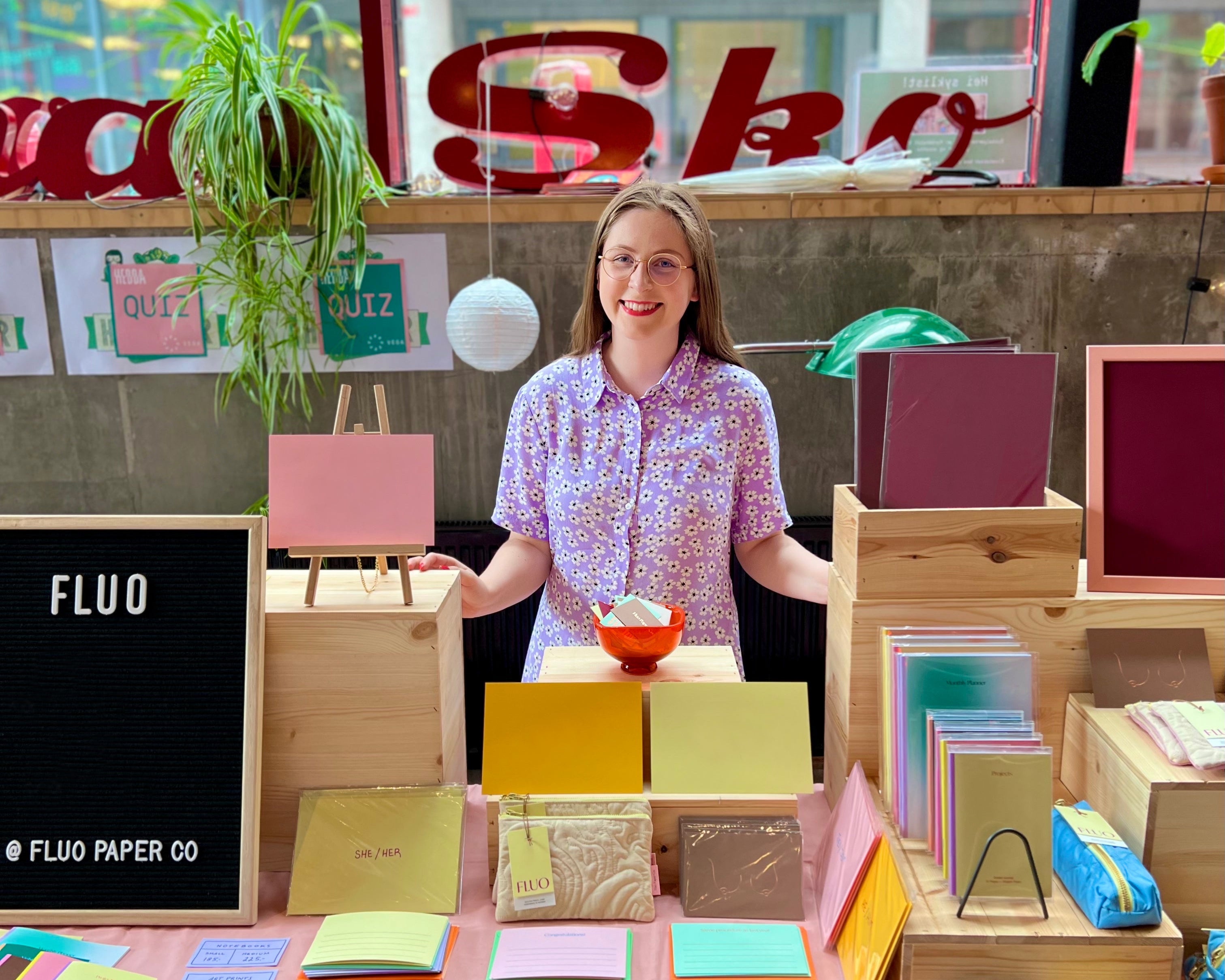 Woman standing behind a table displaying colorful paper products with 'Fluo' branding.