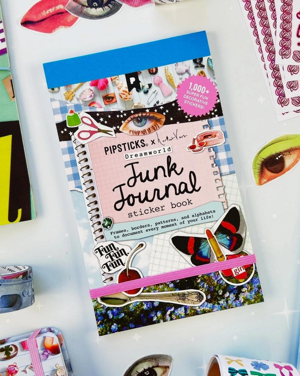 Dreamworld junk journal sticker book with washi tape rolls and loose decorative stickers on a desk