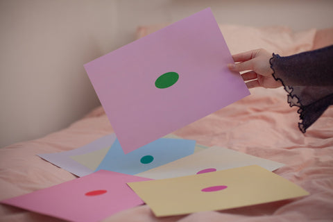 Hand holding a pink sheet of paper with a green oval in the center, depicting a blank mind map. Surrounded by similar sheets in different color combinations.