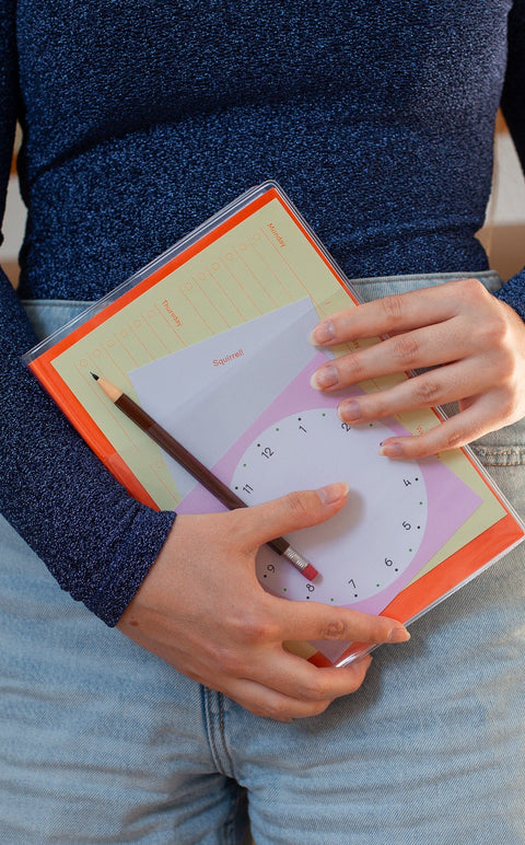 Person holding a notebook by Marjolein Delhaas. The front pocket of the notebook is clear and filled with Fluo memo sheets. The person is wearing a sparkly top, and also holds a mechanical pencil by Penco.