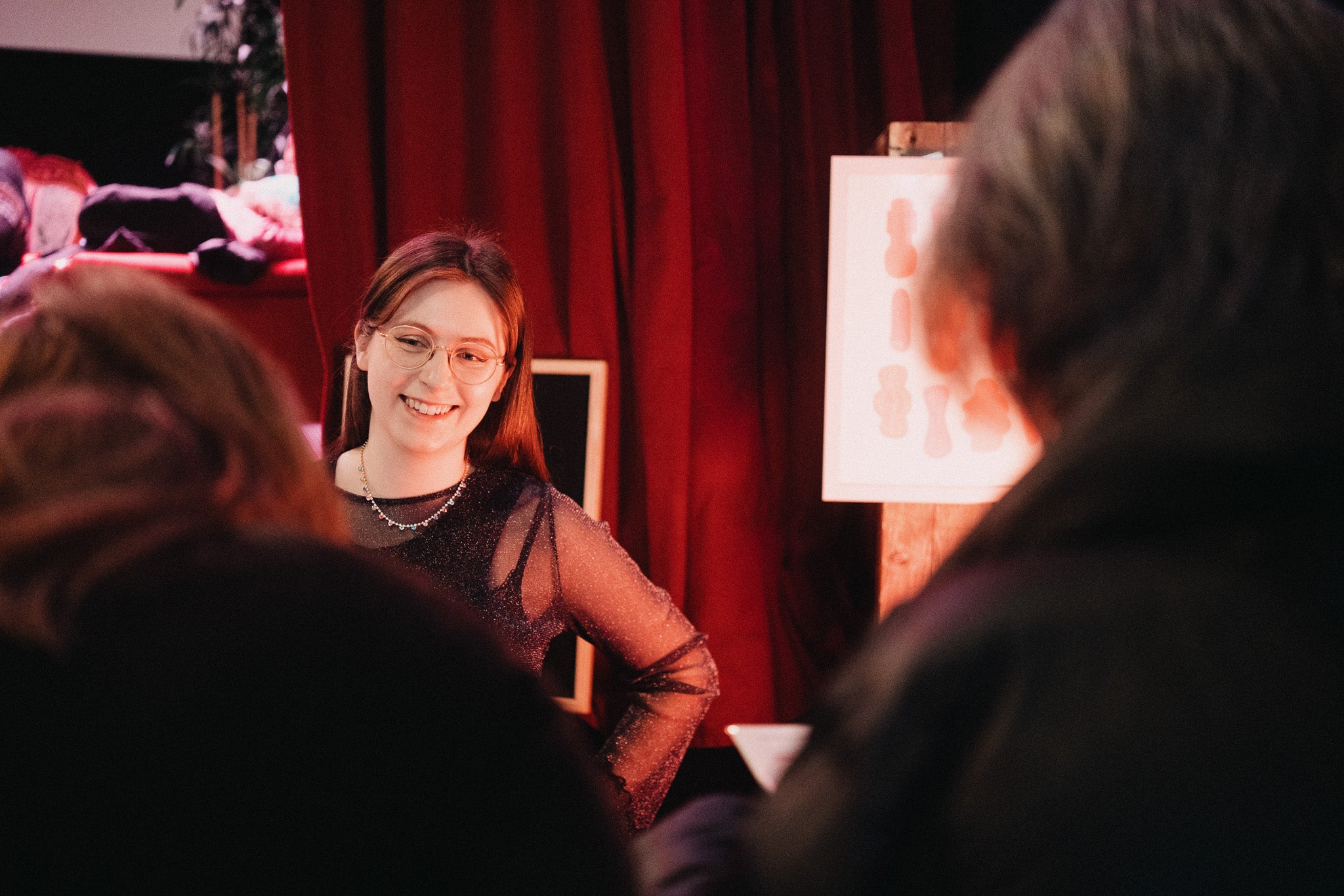 A smiling vendor wearing glasses and a sparkly top stands behind a table of Fluo stationery products at Oslo’s Supermarked. She’s talking to customers with red curtains in the background.