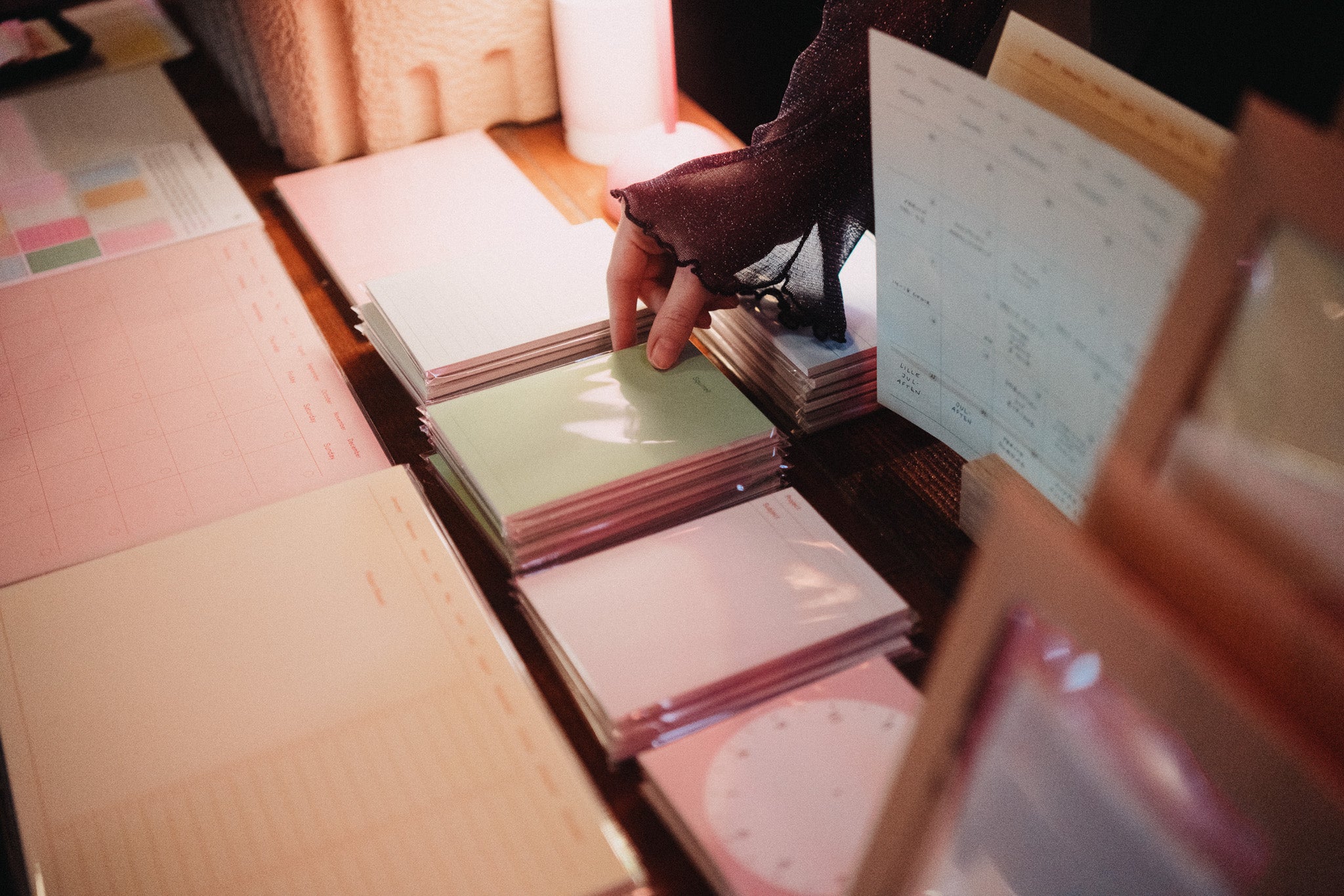 A close-up of someone’s hand picking up pastel-colored notepads from a display of Fluo planners and stationery at Oslos Supermarked.