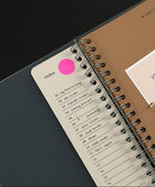 Spiral-bound notebook with an index page and a pink dot on a black background