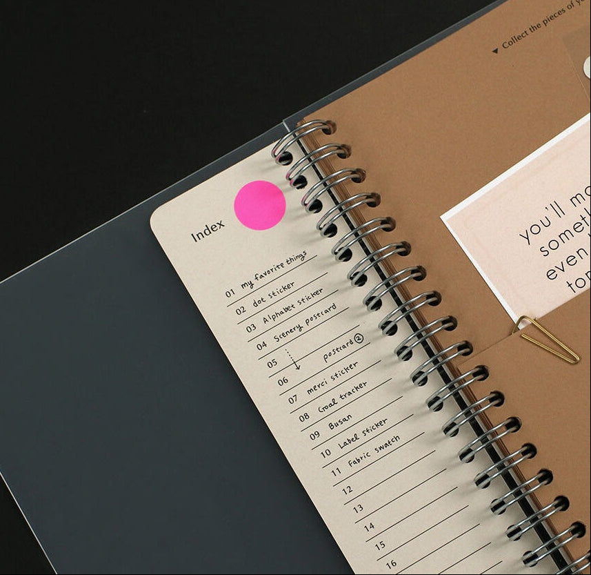 Spiral-bound notebook with an index page and a pink dot on a black background
