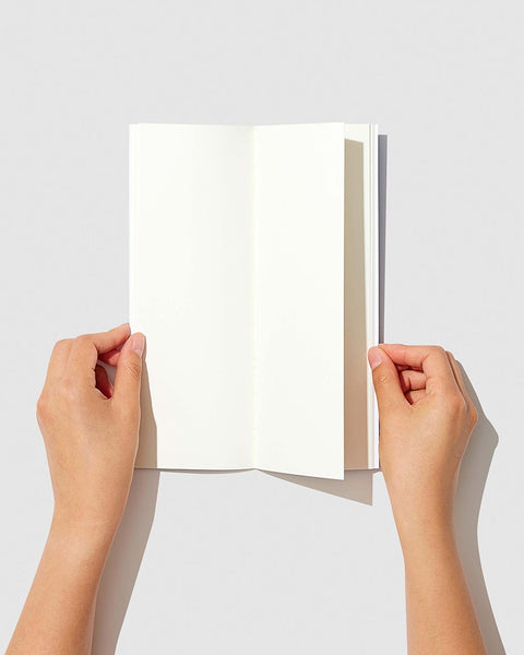 Two hands holding a tall slim notebook with plain white pages against a light gray background