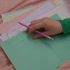Hand holding a pink pencil resting on colorful memo sheets designed for making  analogue vision boards.