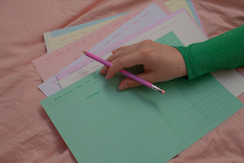 Hand holding a pink pencil resting on colorful memo sheets designed for making  analogue vision boards.
